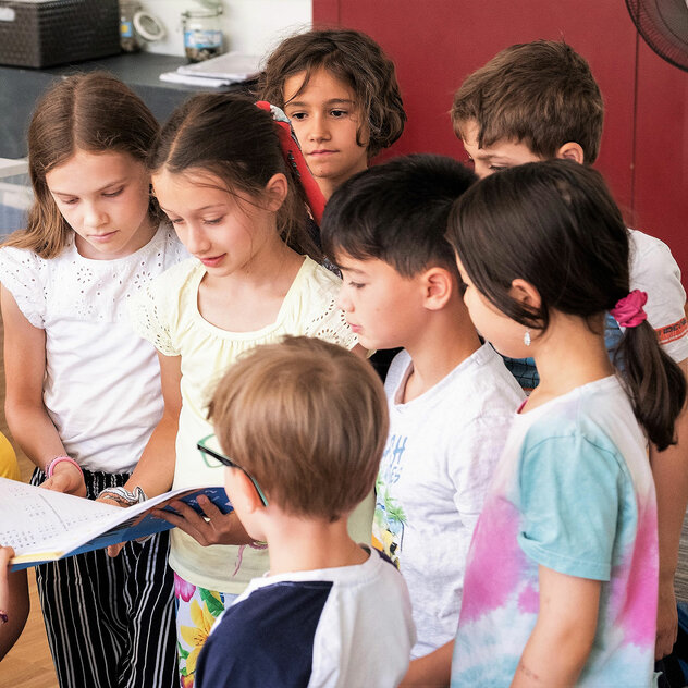 A group of primary school children stand close together and look into a notebook.	