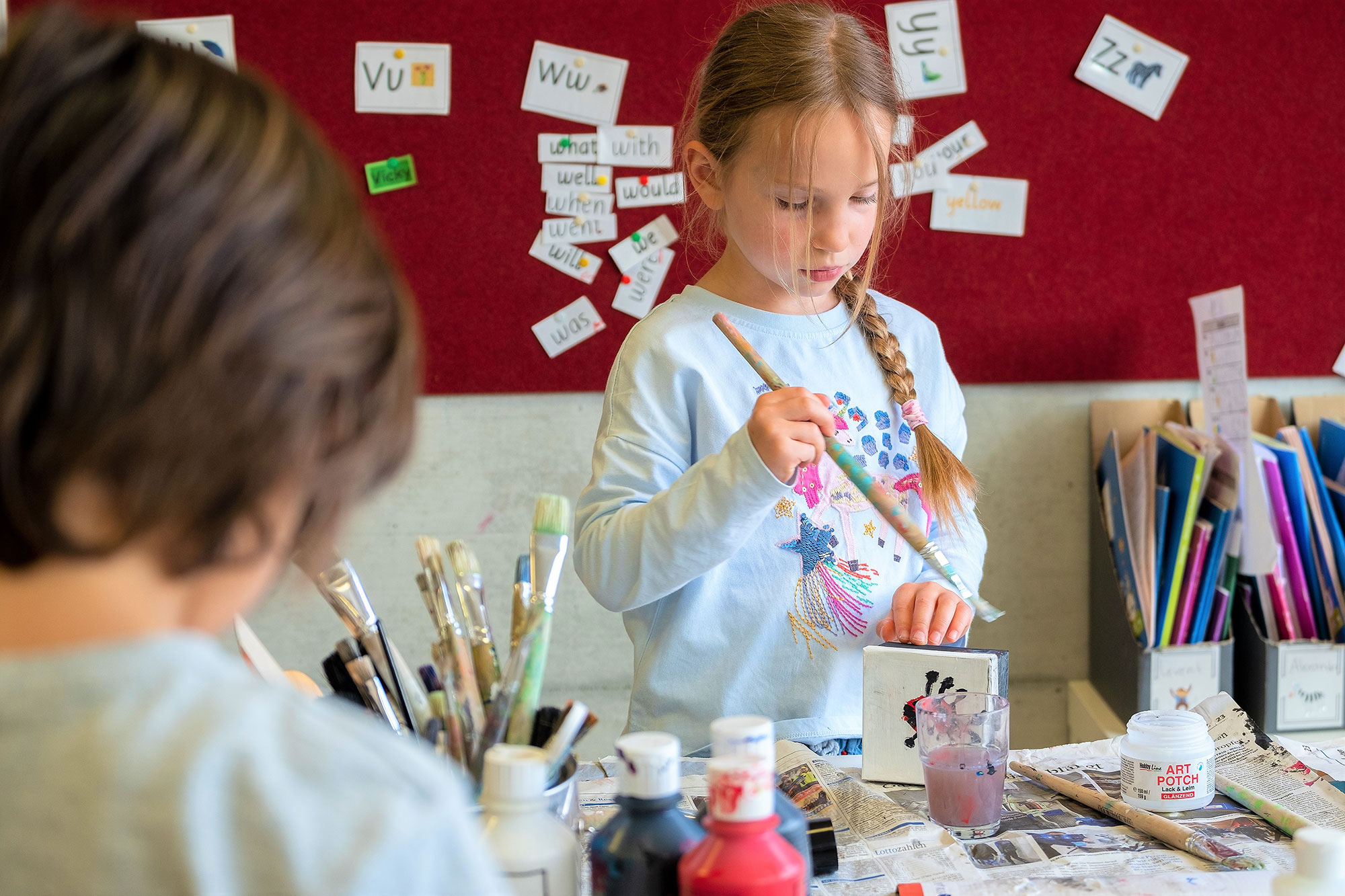 A little girl is holding a paintbrush and working on an arts project.	