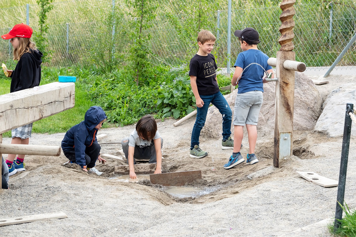 Kinder spielen draussen auf dem Abenteuerspielplatz der Schule. 	