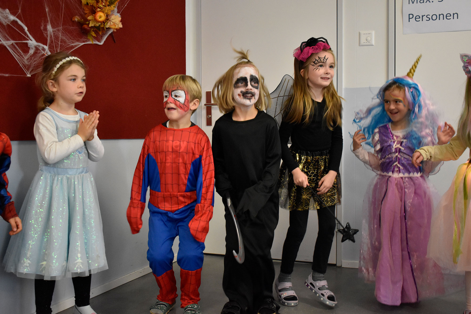 Schülerinnen und Schüler feiern Halloween und tragen bunte Kostäume. Einige sind als Spiderman oder Hexen verkleidet.	