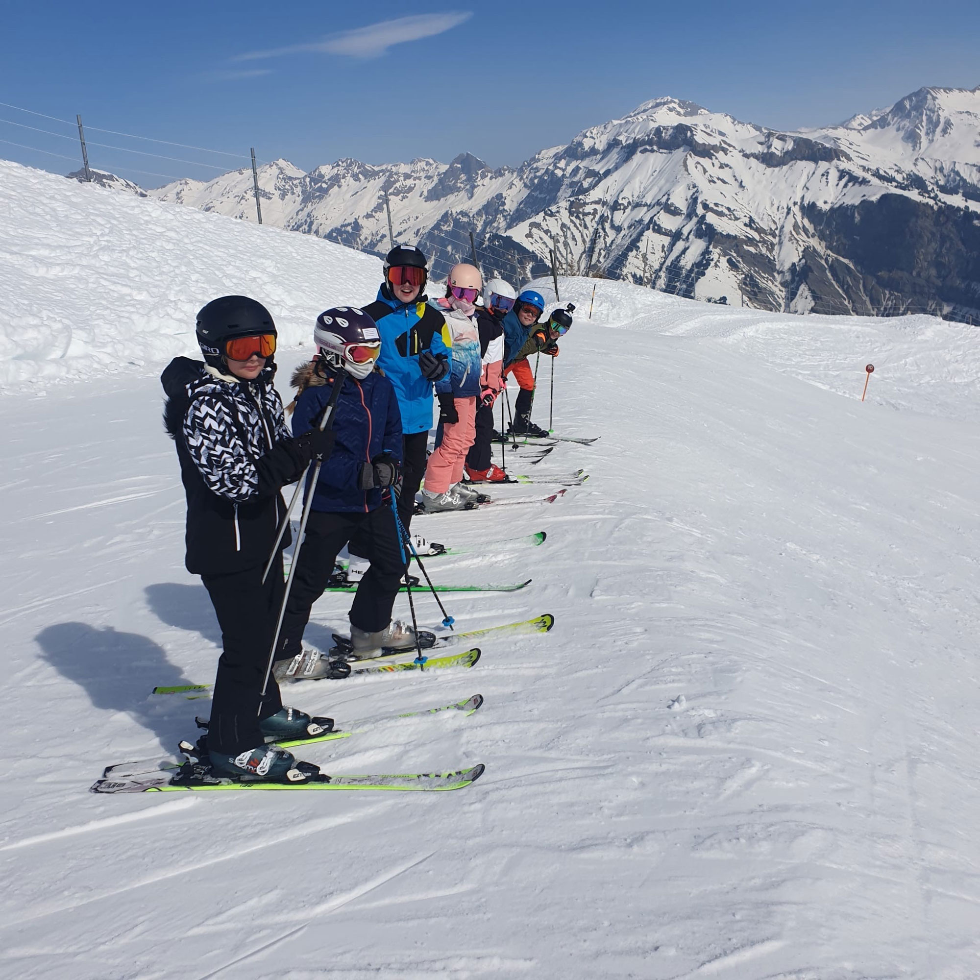 Students stand side by side on skis on the ski slope on ski day.	