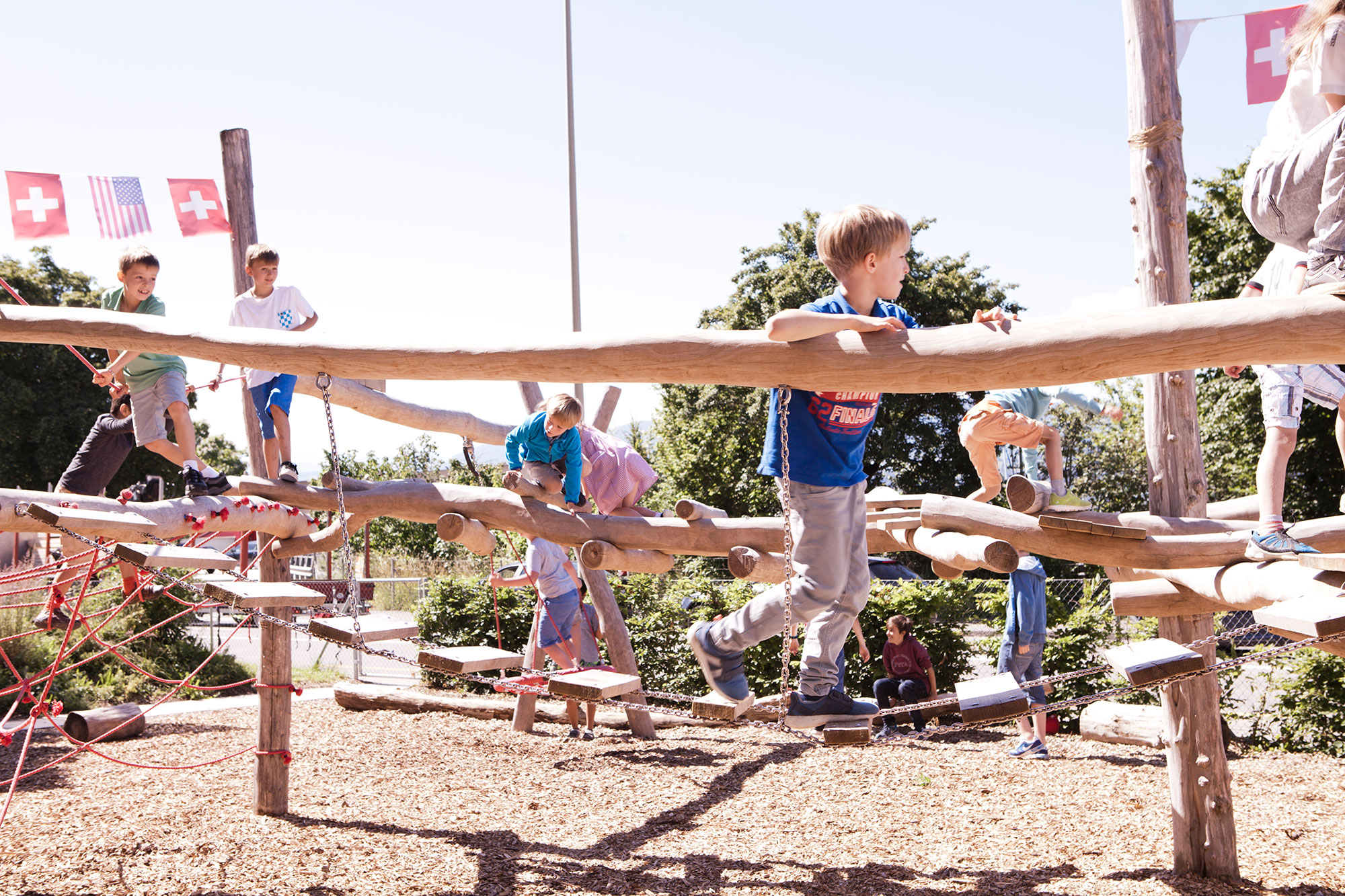 Kinder spielen draussen auf dem Pausenplatz auf dem Klettergerüst bei sonnigem Wetter.	