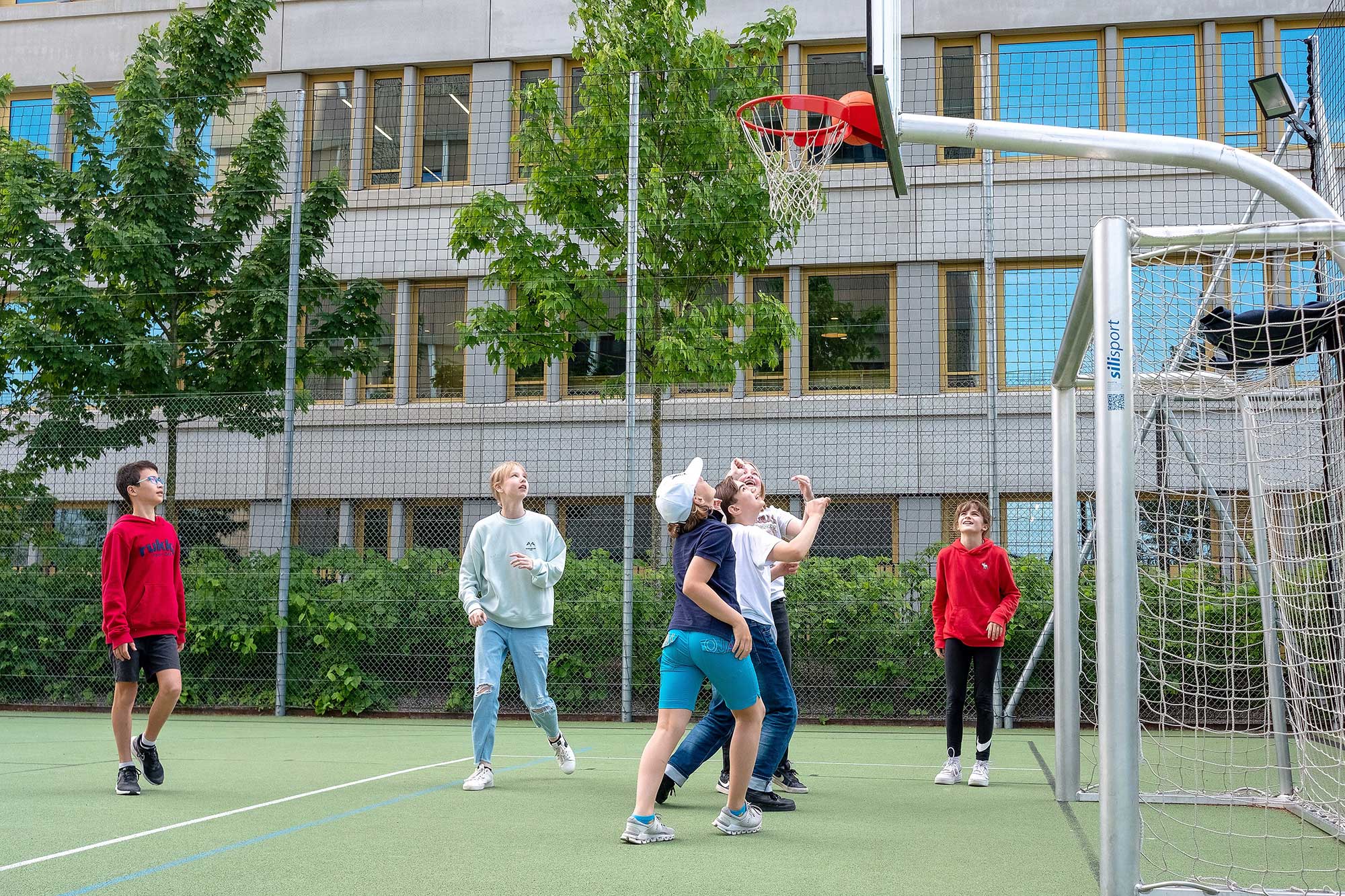 Eine Gruppe von Schülerinnen und Schülern spielt Basketball auf dem Sportplatz.	