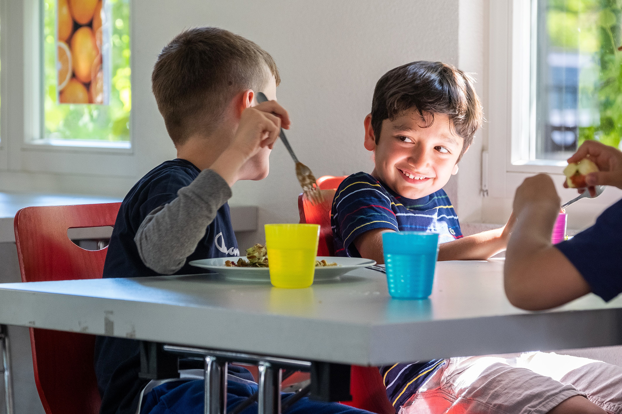 Two little boys sit in the school cafeteria and eat lunch together.	