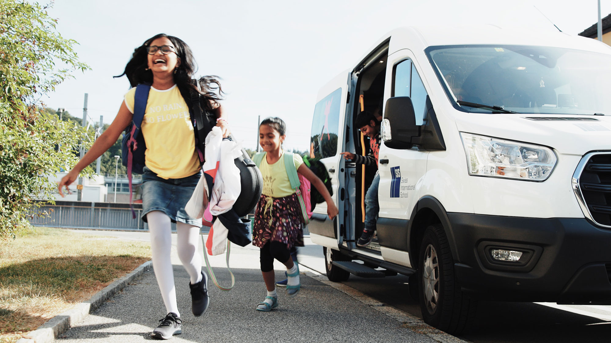 Girls get off the school bus laughing and run to the school entrance.	