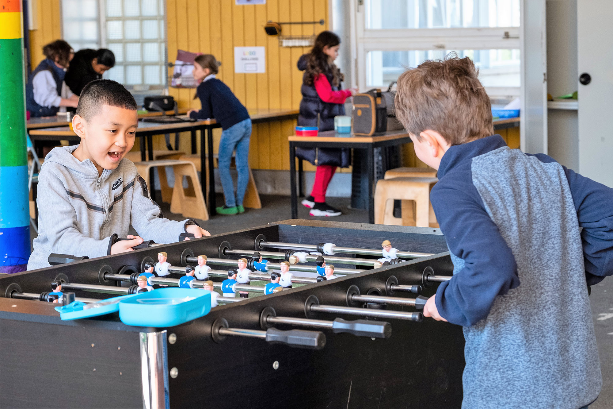 Two boys are playing table football in the large playground.	