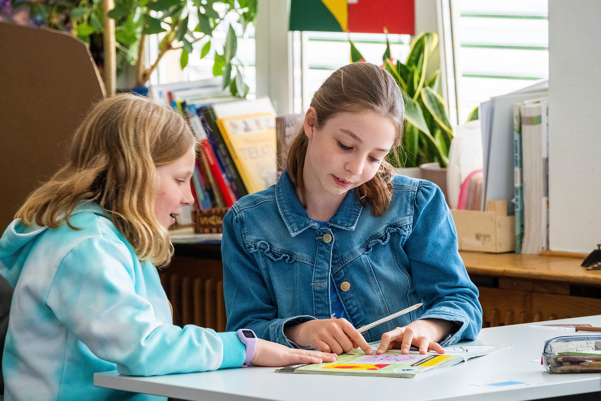 Two older primary school girls sit at the table and work together on a task.	