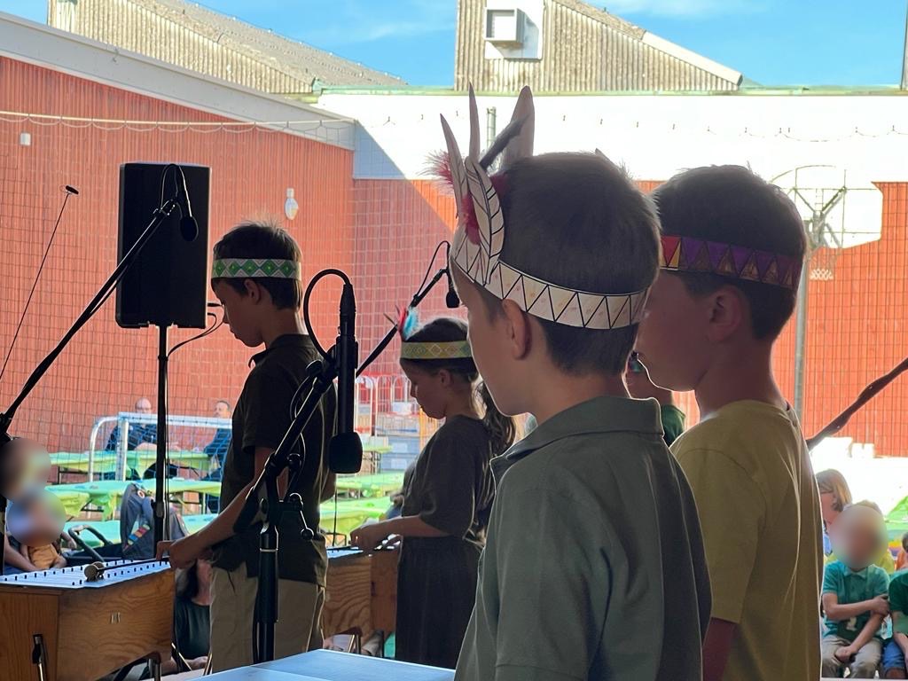 Vier Jungen spielen gemeinsam ein Musiksttück mit einem Indianerhut auf dem Kopf.	