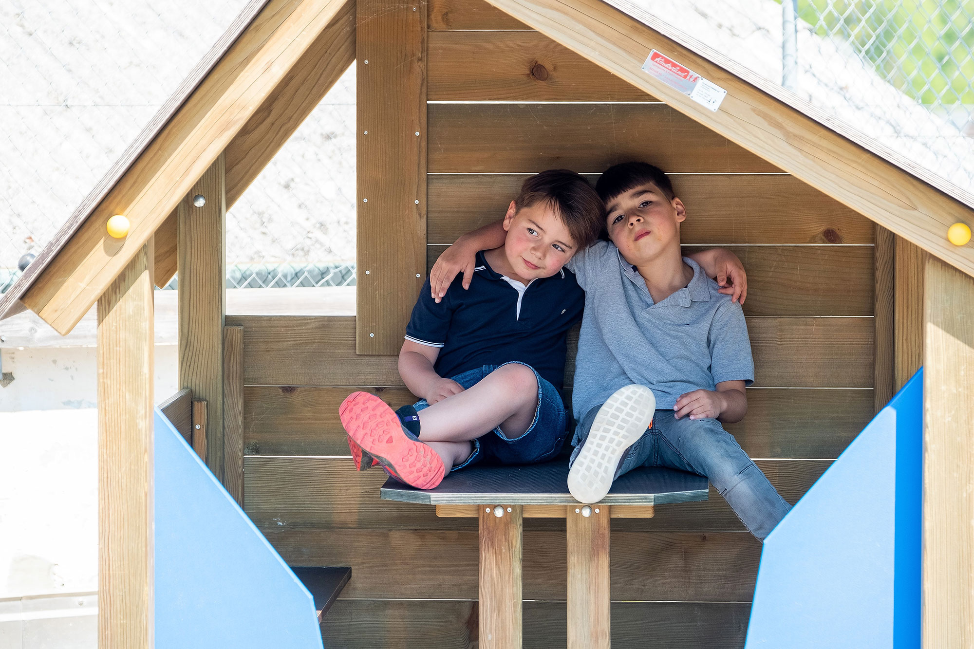 Two boys sit in a wooden house and hug each other.	