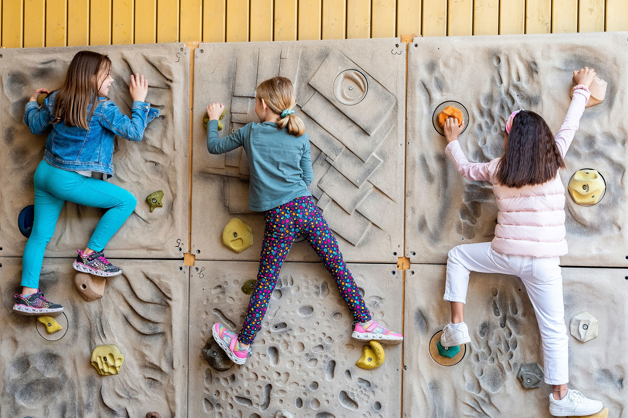 Three girls hold on to the climbing wall.	