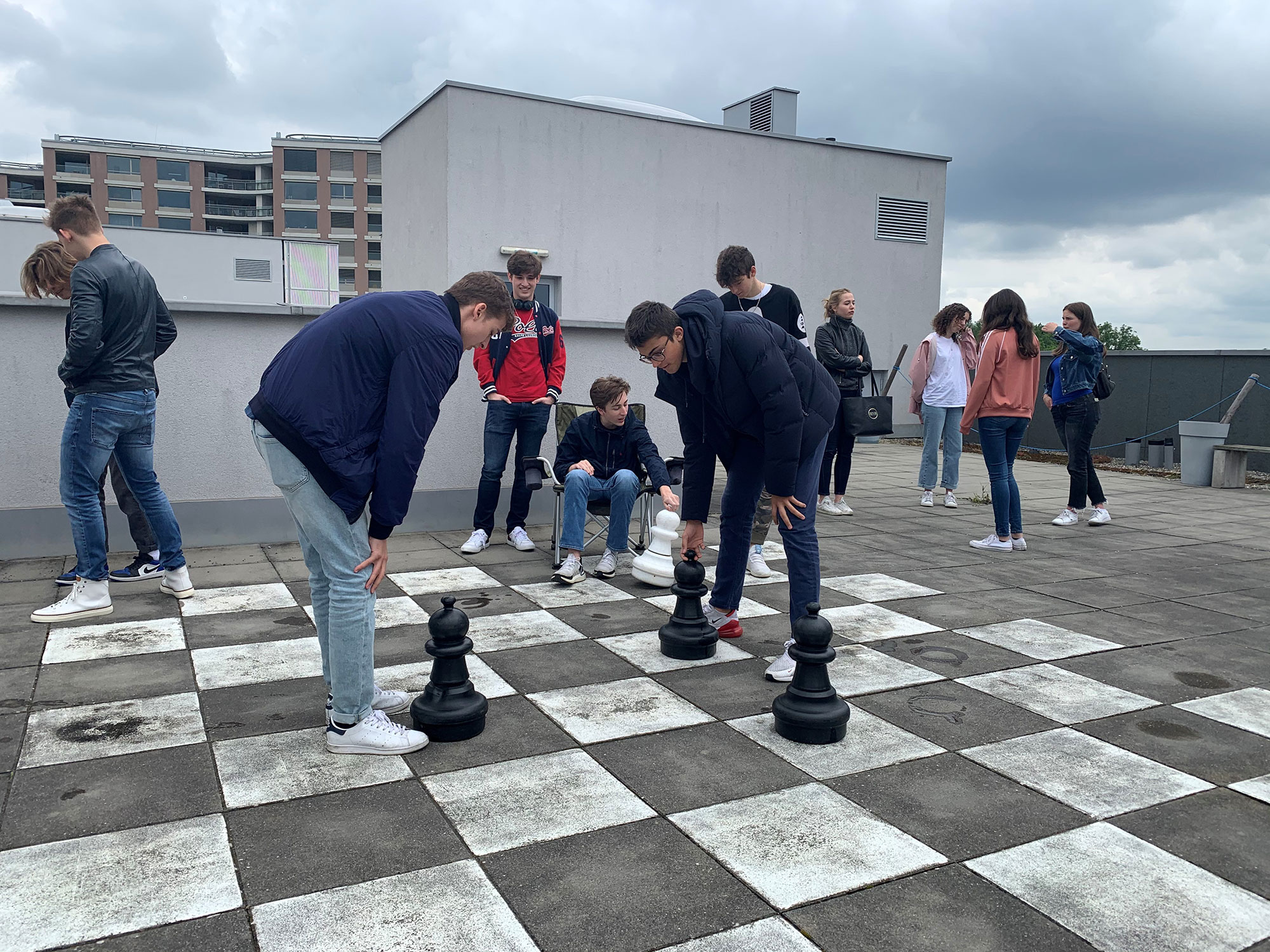 Ältere Studenten spielen auf der Schuldachterrasse Schach auf dem Boden.	
