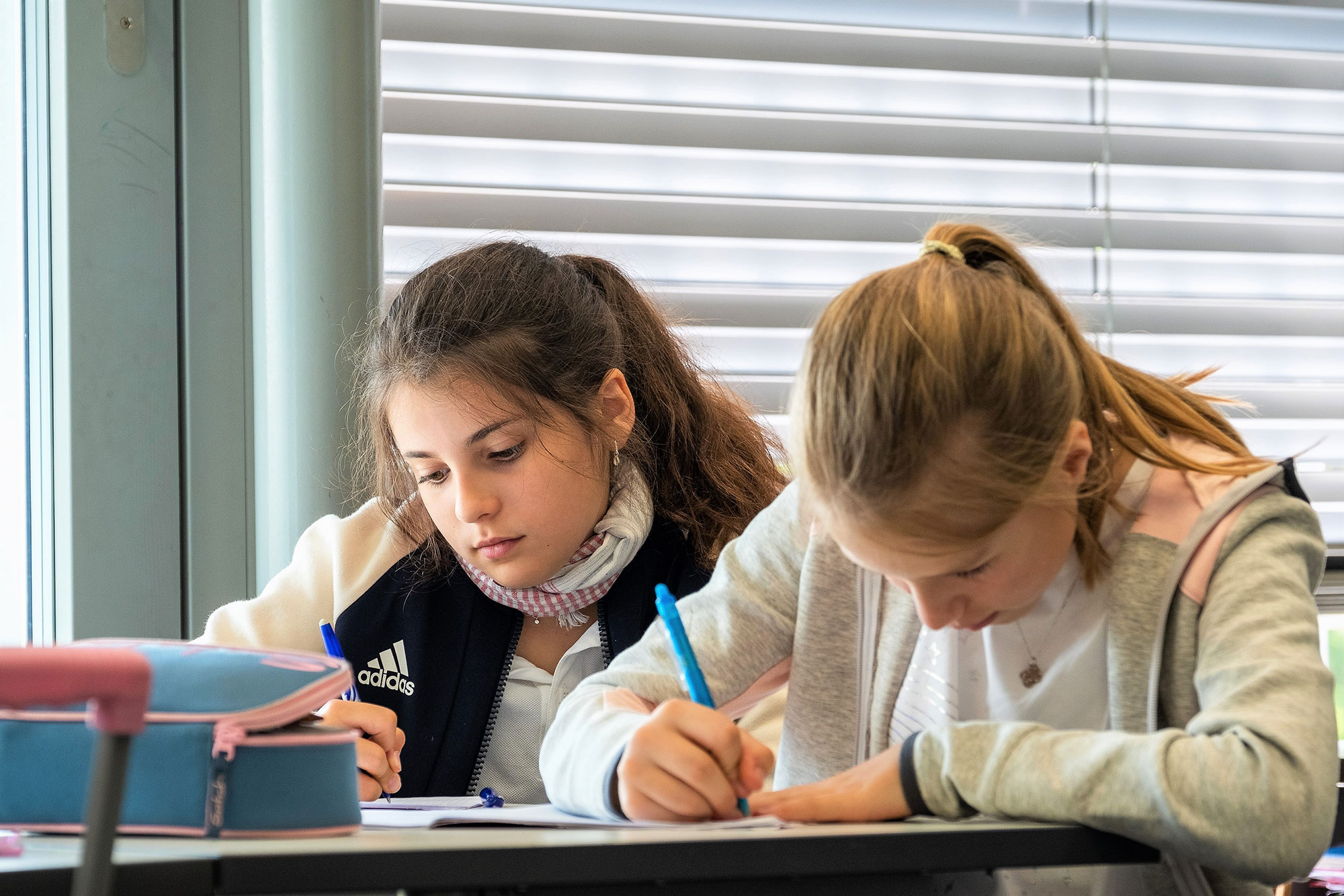 Two older primary school girls sit at their desks and write.	