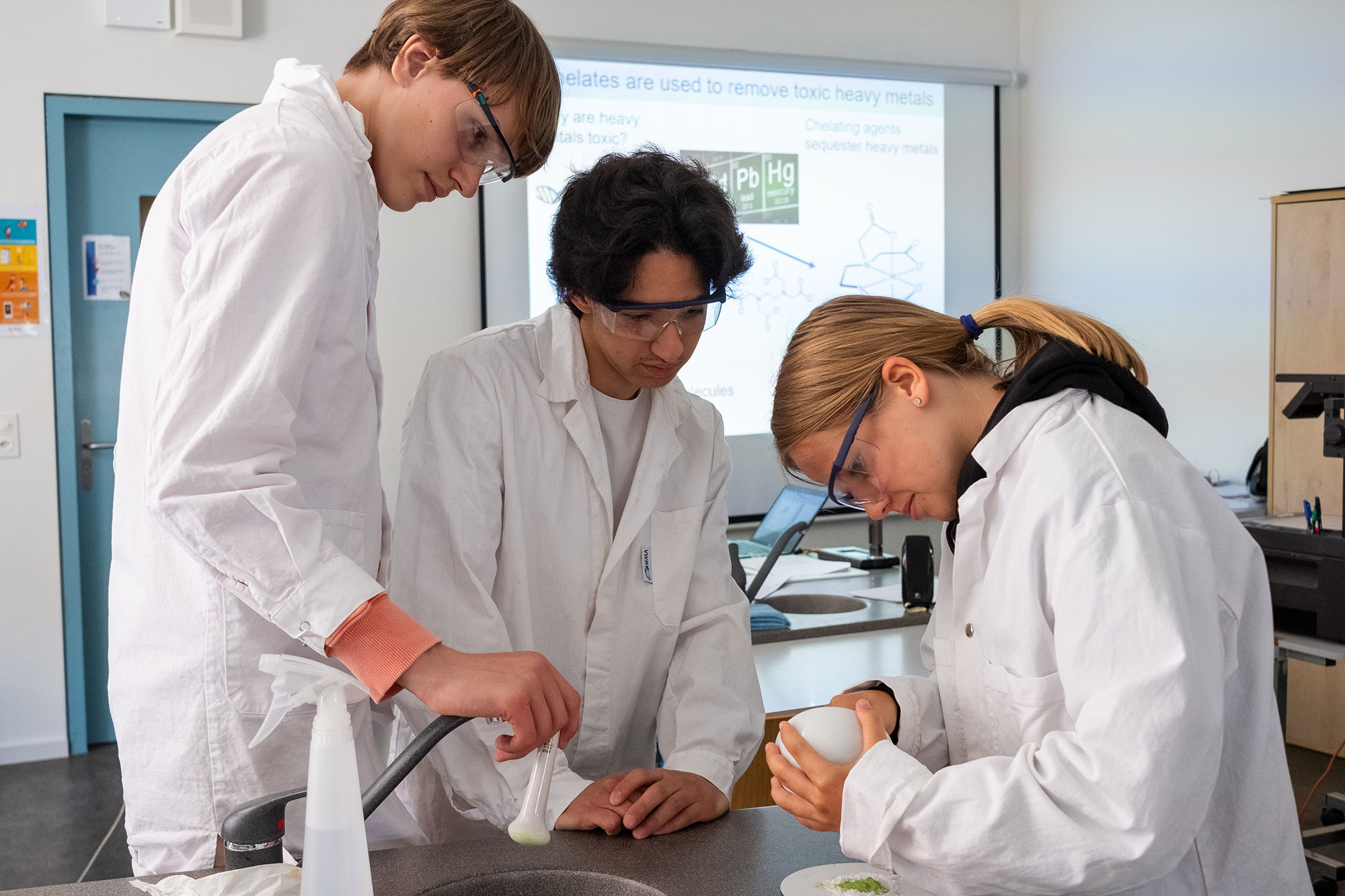 Two male students and a female student are experimenting in the laboratory and are wearing white coats.	