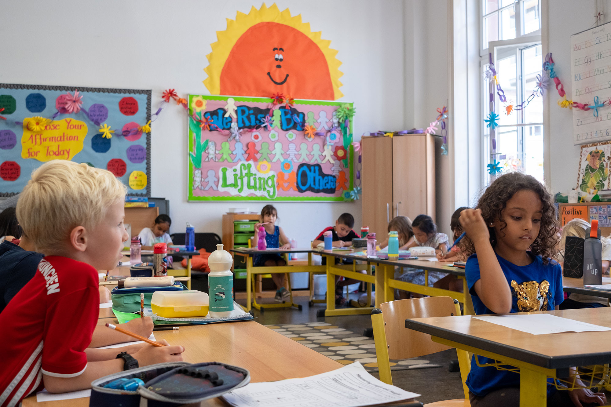 Kindergartenkinder sitzen an ihren Tischen im farbenfrohen Unterrichtszimmer.	
