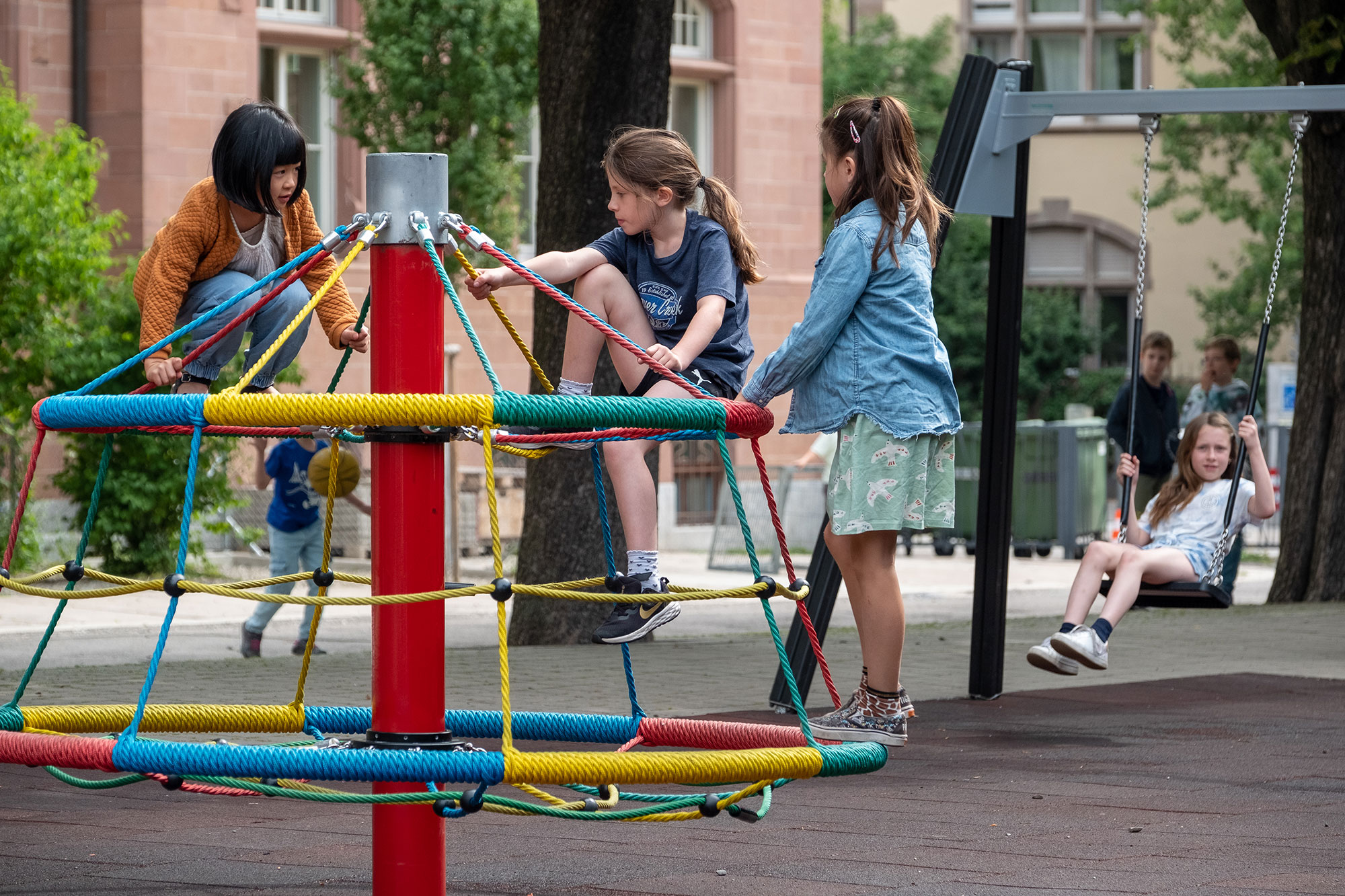 Drei Mädchen spielen auf dem Spielplatz auf einem runden Karussell.	