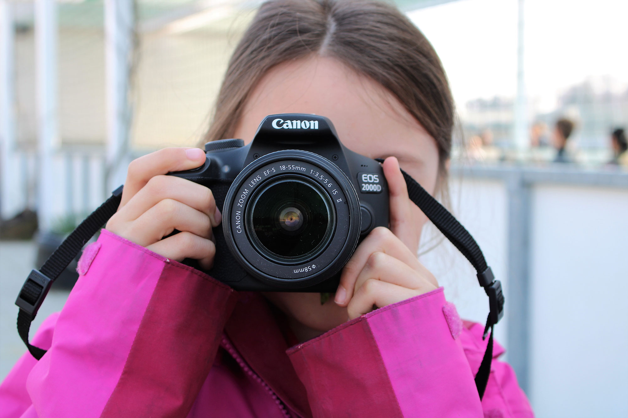 A girl photographs the viewer with a large camera. Her face is covered by the camera.	
