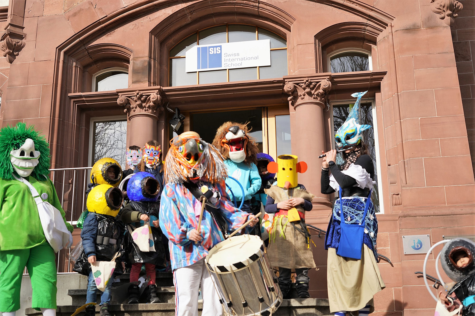 Dressed-up children stand in front of the school entrance of SIS Basel to celebrate the Basel Fastnacht.	