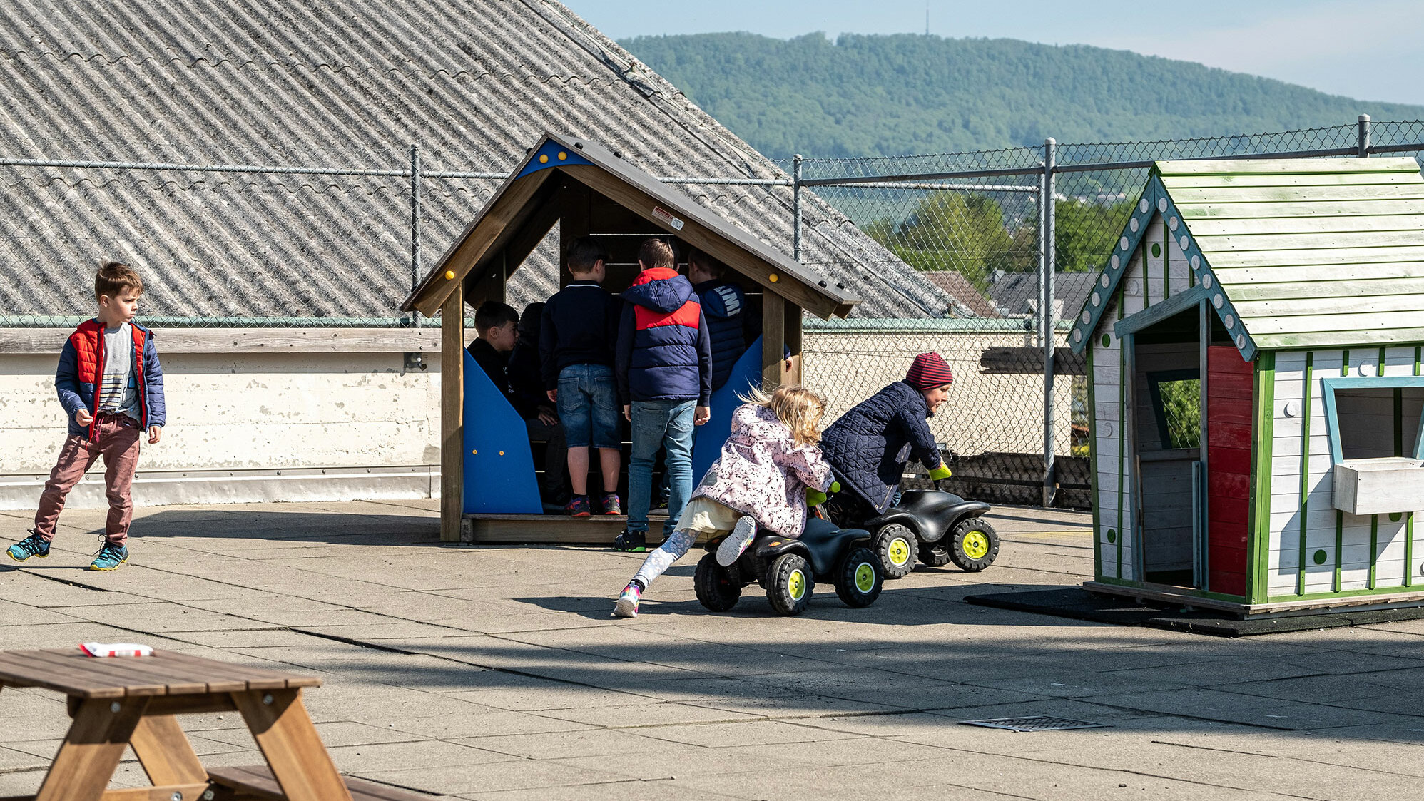 Ein Junge und ein Mädchen aus dem Kindergarten spielen mit einem Bobbycar auf der geschützten Terrasse.	