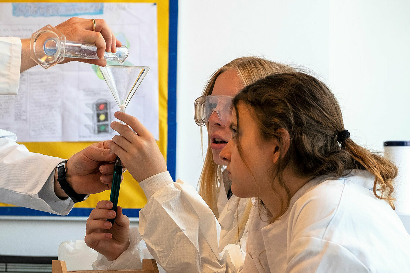 Ein Lehrer zeigt zwei Schülerinnen ein Experiment im Labor.	