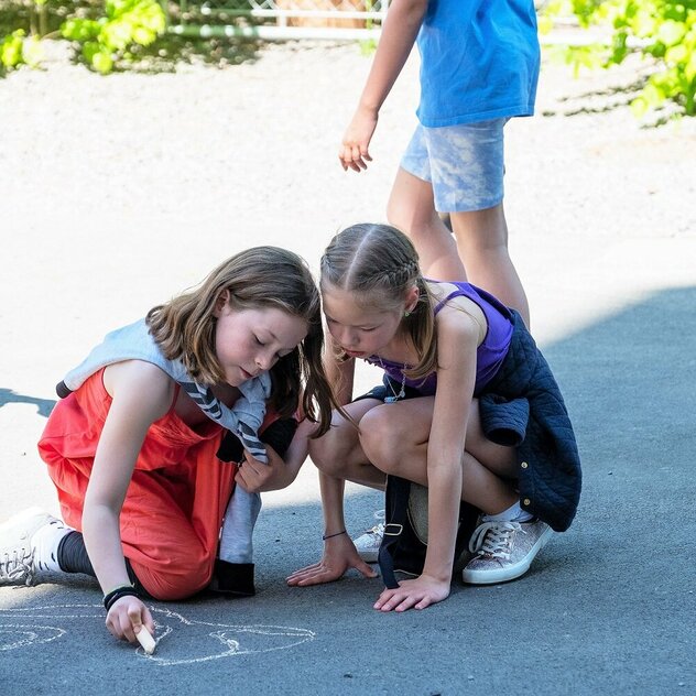 Two girls are drawing something on the floor outside.