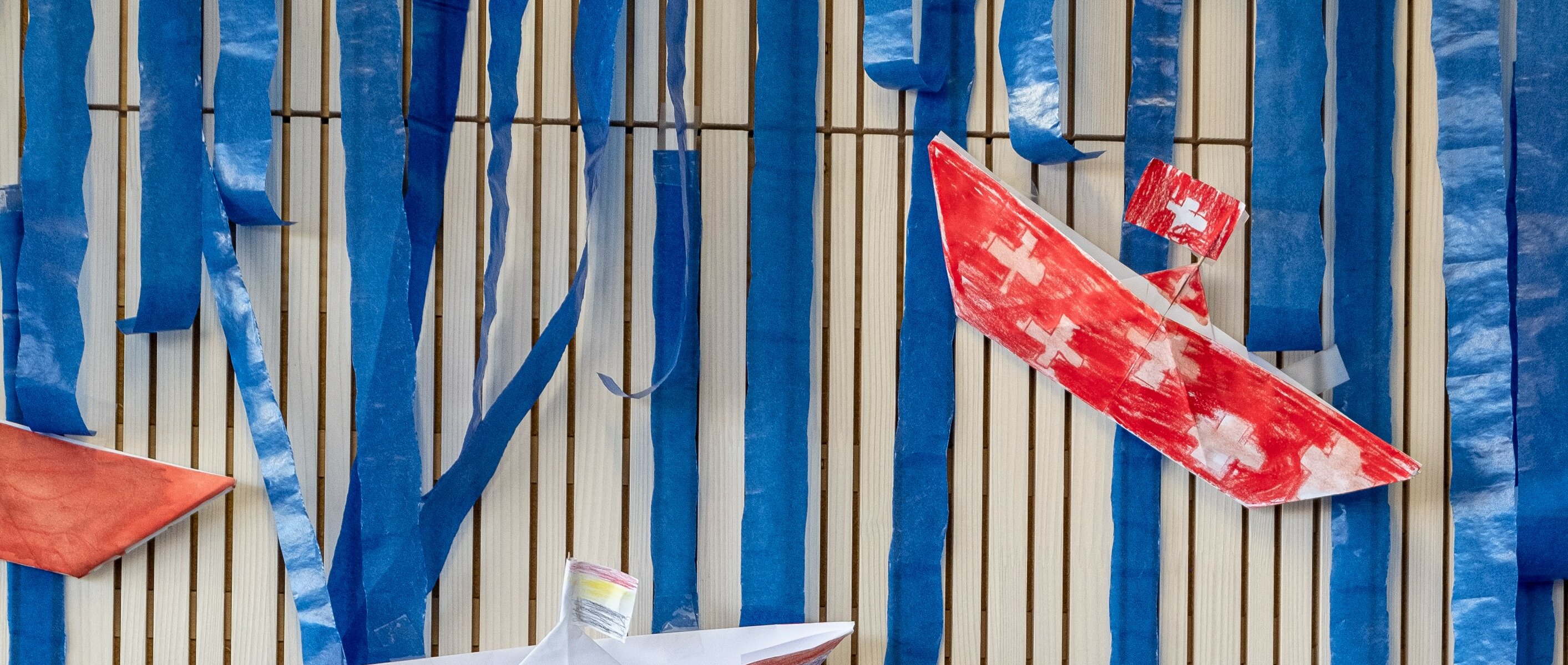 Self-made, painted paper boats hang on the wall as decoration. One of the boats is painted with the Swiss flag.