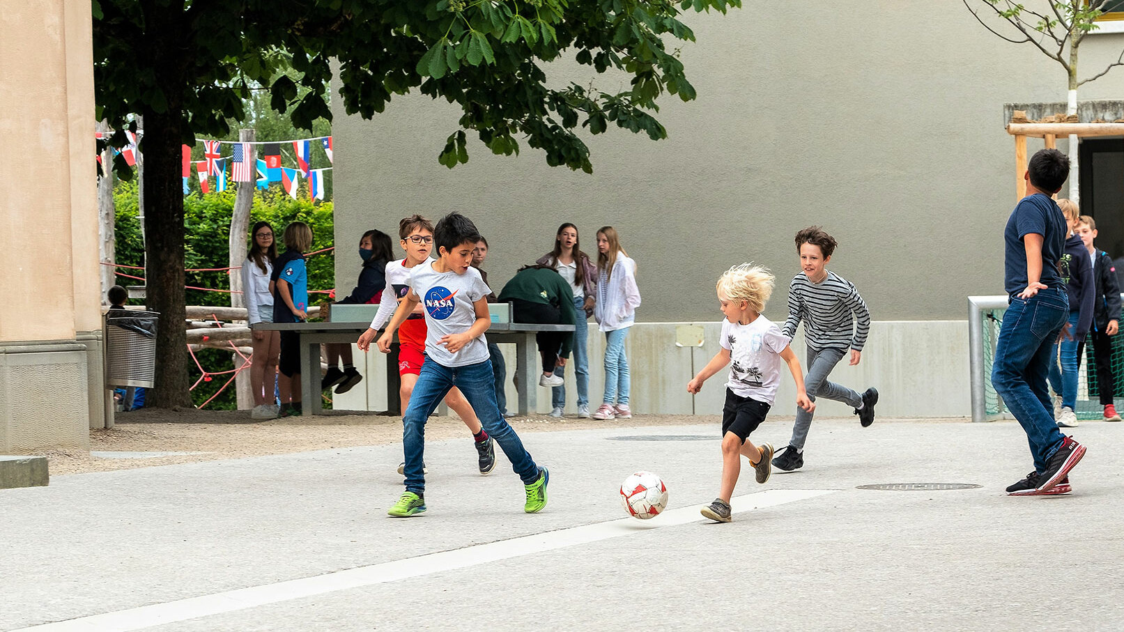 A group of children are playing football outside on the playground of the school. 	