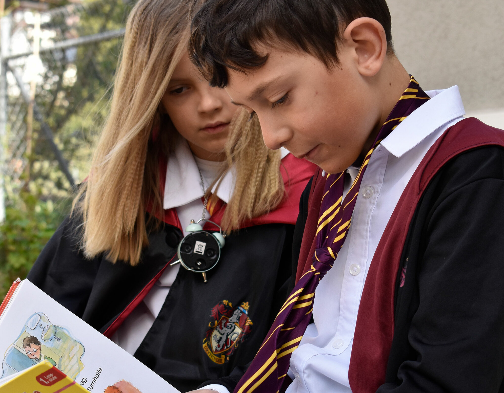 Ein Junge und ein Mädchen sind verkleidet als Harry Potter und lesen gemeinsam ein Buch am World Book Day.	