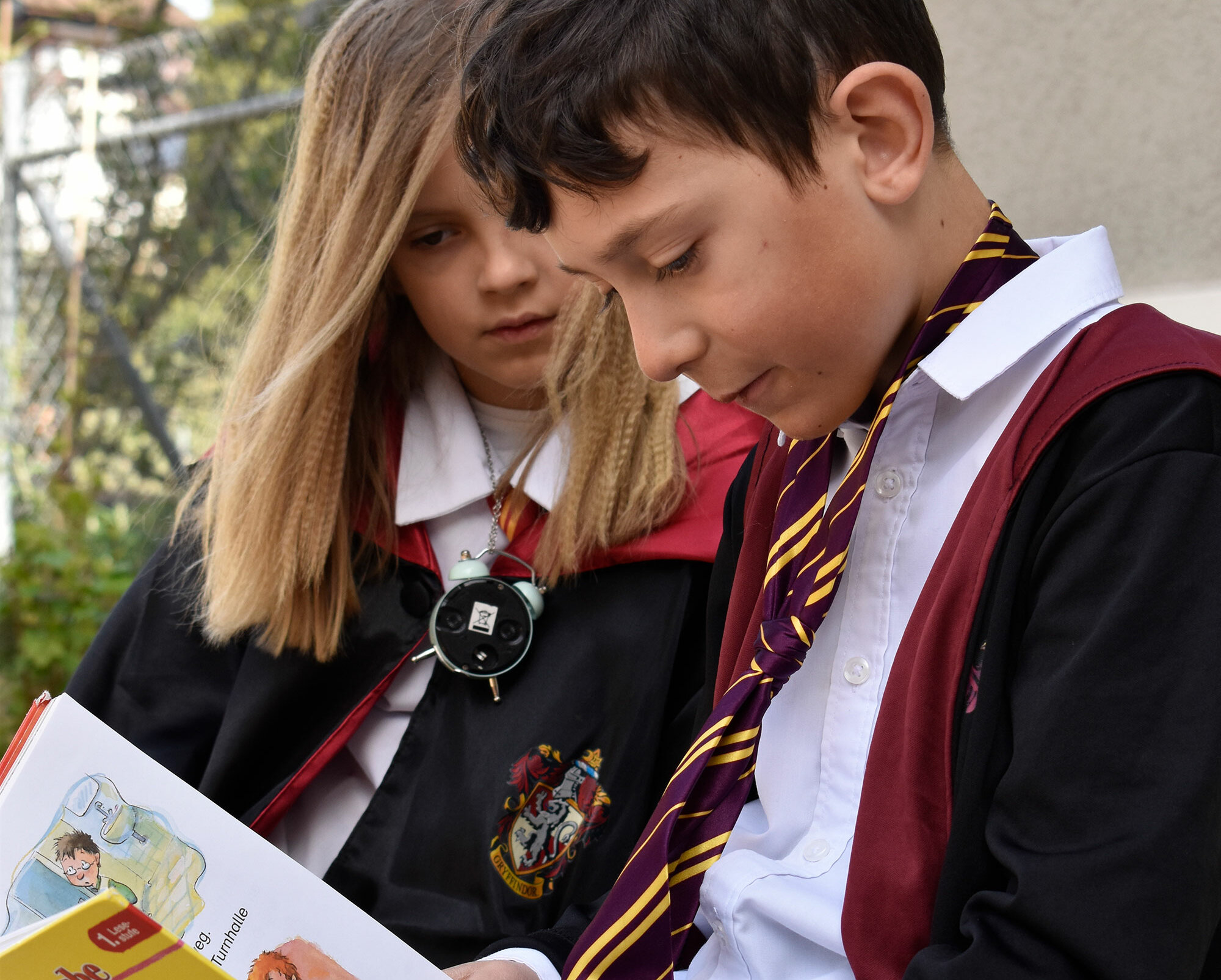 A boy and a girl are dressed up as Harry Potter and read a book together on World Book Day.	