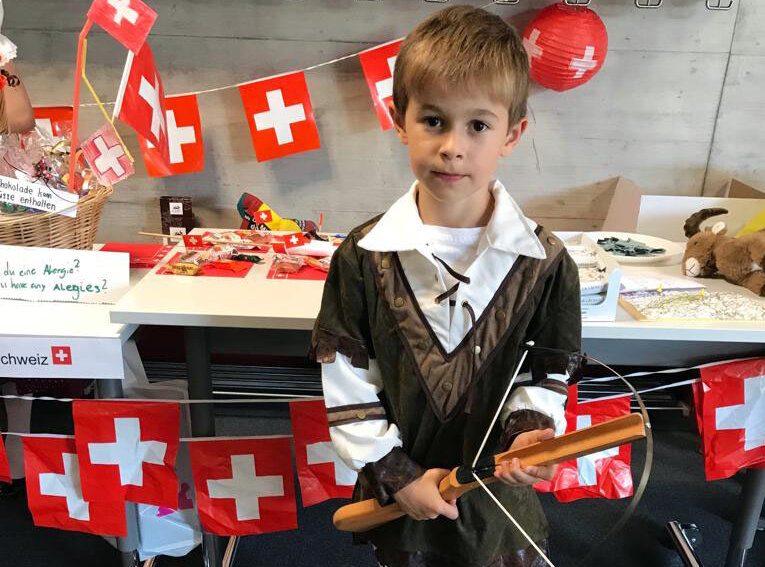 A little boy is dressed as Willhelm Tell and represents Switzerland. In the background you can see many Swiss flags.	