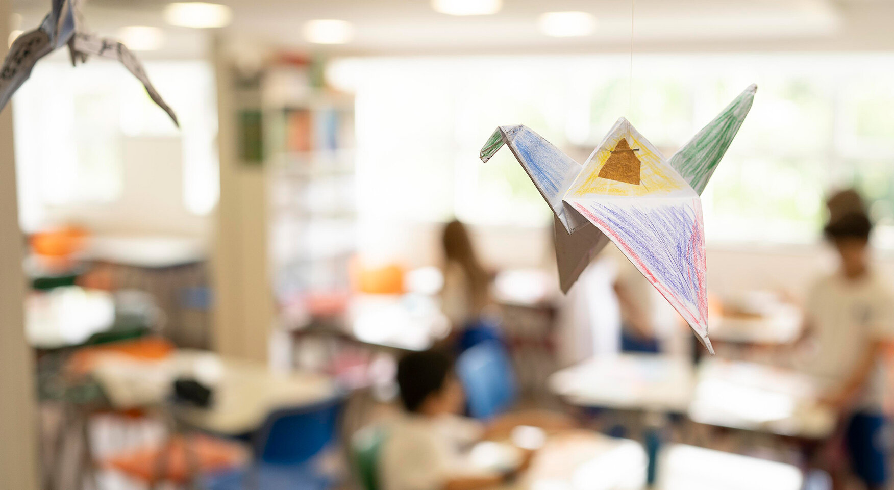 A handmade, painted origami crane hangs in the classroom, which fades into the background.