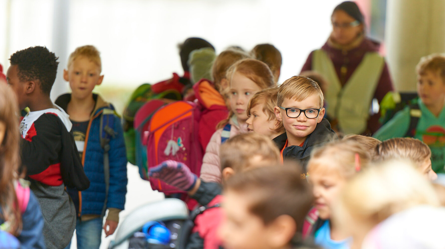 In a group of students, a boy with glasses looks directly into the camera.