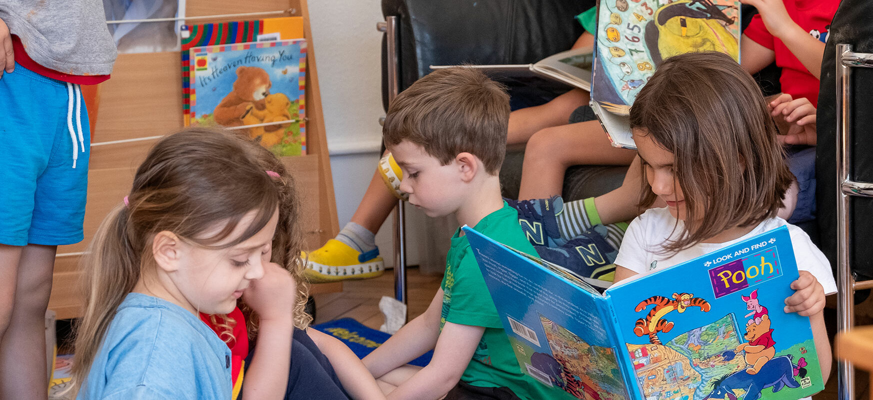Kindergartenkinder sind in der Bibliothek. Ein kleiner Junge ist im Vordergrund, er öffnet ein Buch.	
